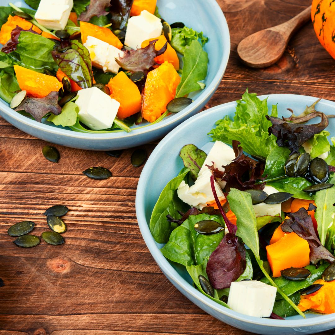 Nourish bowl with roasted pumpkin, quinoa, greens, avocado, pumpkin seeds, and salmon, drizzled with tahini dressing.