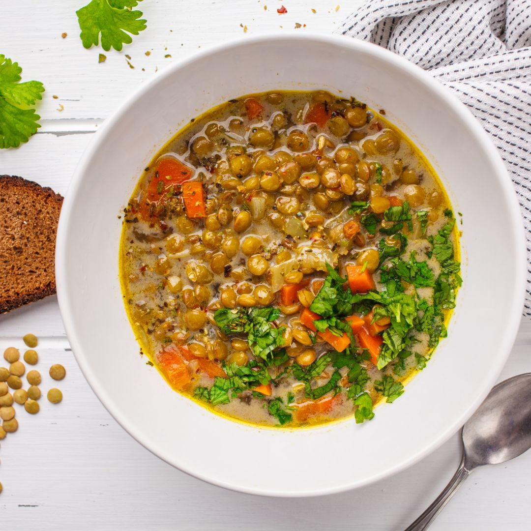 Bowl of hearty lentil and spinach stew with herbs on top, served with wholegrain bread.